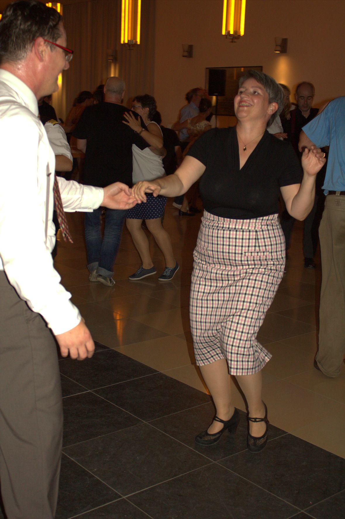 Fotografie einer Tanzfläche. Im Vordergrund sieht man eine Frau & einen Mann, die gemeinsam Lindy Hop tanzen.